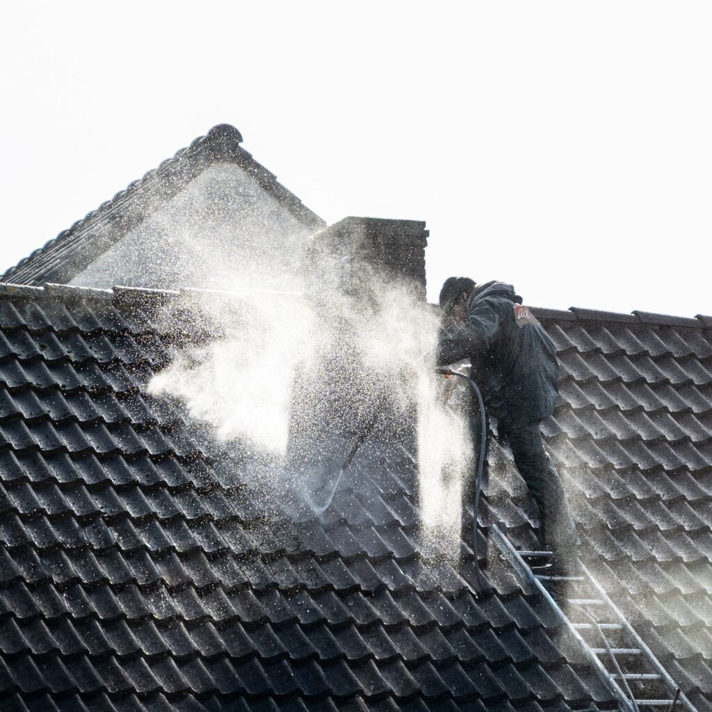Worker pressure washing roof tiles during surface preparation